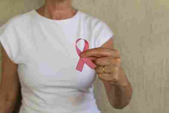 Woman in white t-shirt holds a pink breast cancer awareness ribbon to promote prevention and women's health. 