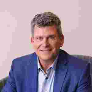 Stephen White in a navy sports coat is sitting down, portrait. Close-up. Chief Operating Officer