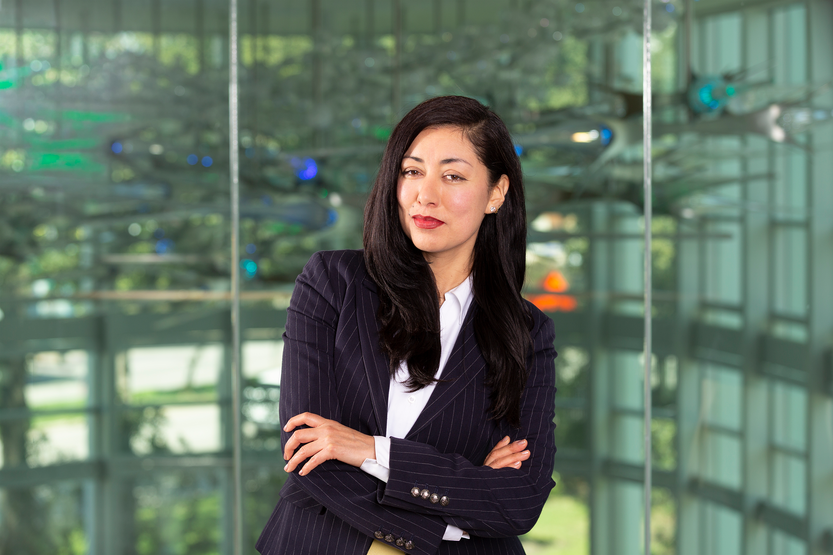 Headshot of Rosa Escobedo in a pinstriped jacket, standing in front or a large glass neuro sculpture at Center for BrainHealth.
