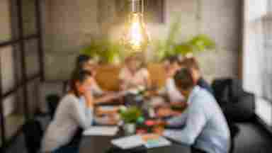 Businesspeople working together in the background with a light bulb in camera focus (indicating new idea).