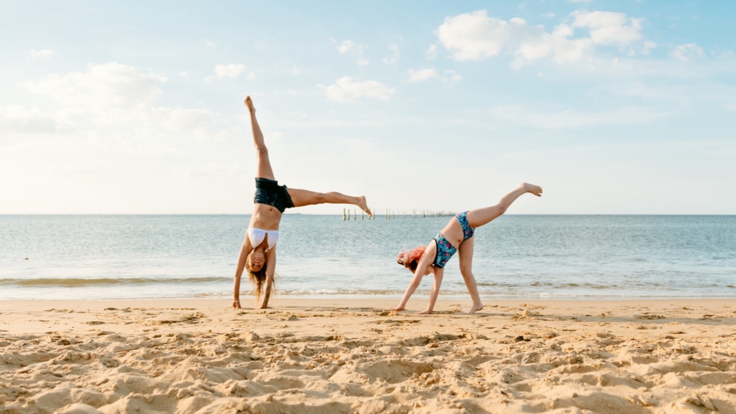 Young people practicing cartwheels on the beach.