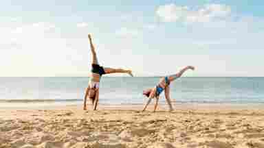Young people practicing cartwheels on the beach.