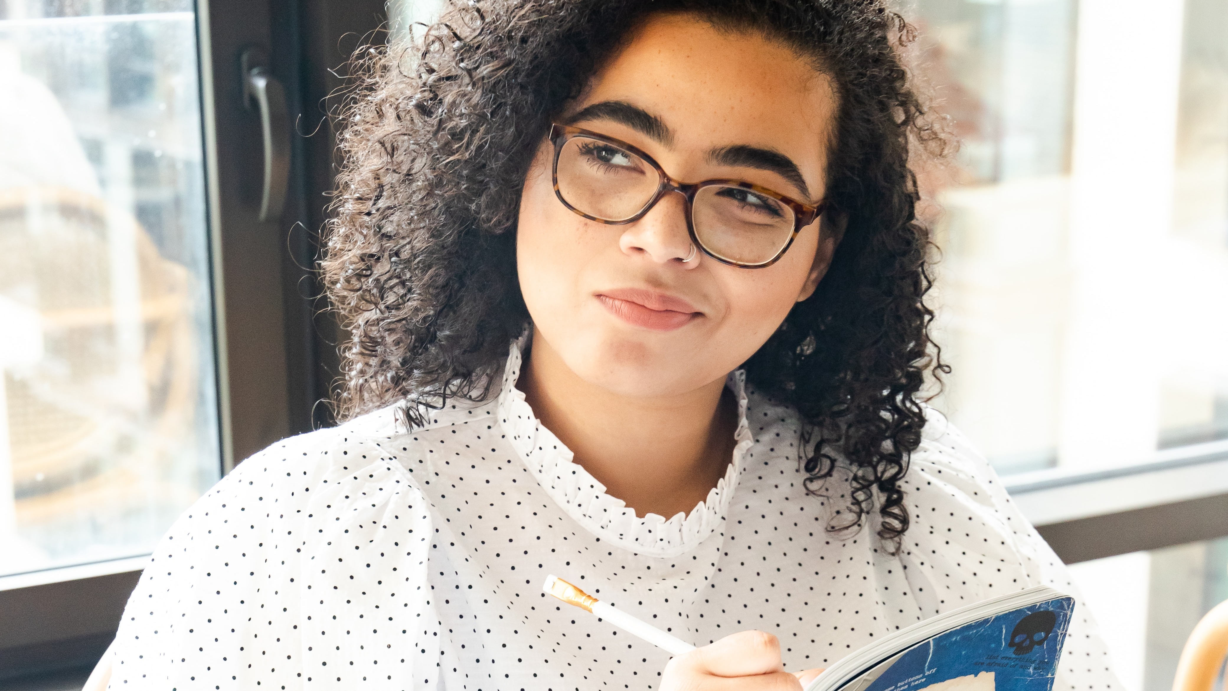 A young woman of color smiling as she writes in a notebook. 