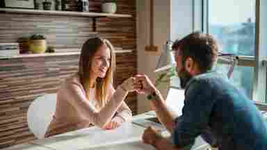 A young woman and man are fist bumping together while sitting down in an office setting.