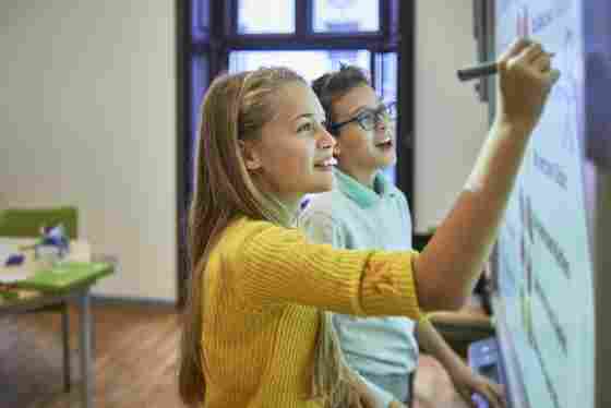 Two teenage friends work together on a project in their classroom.