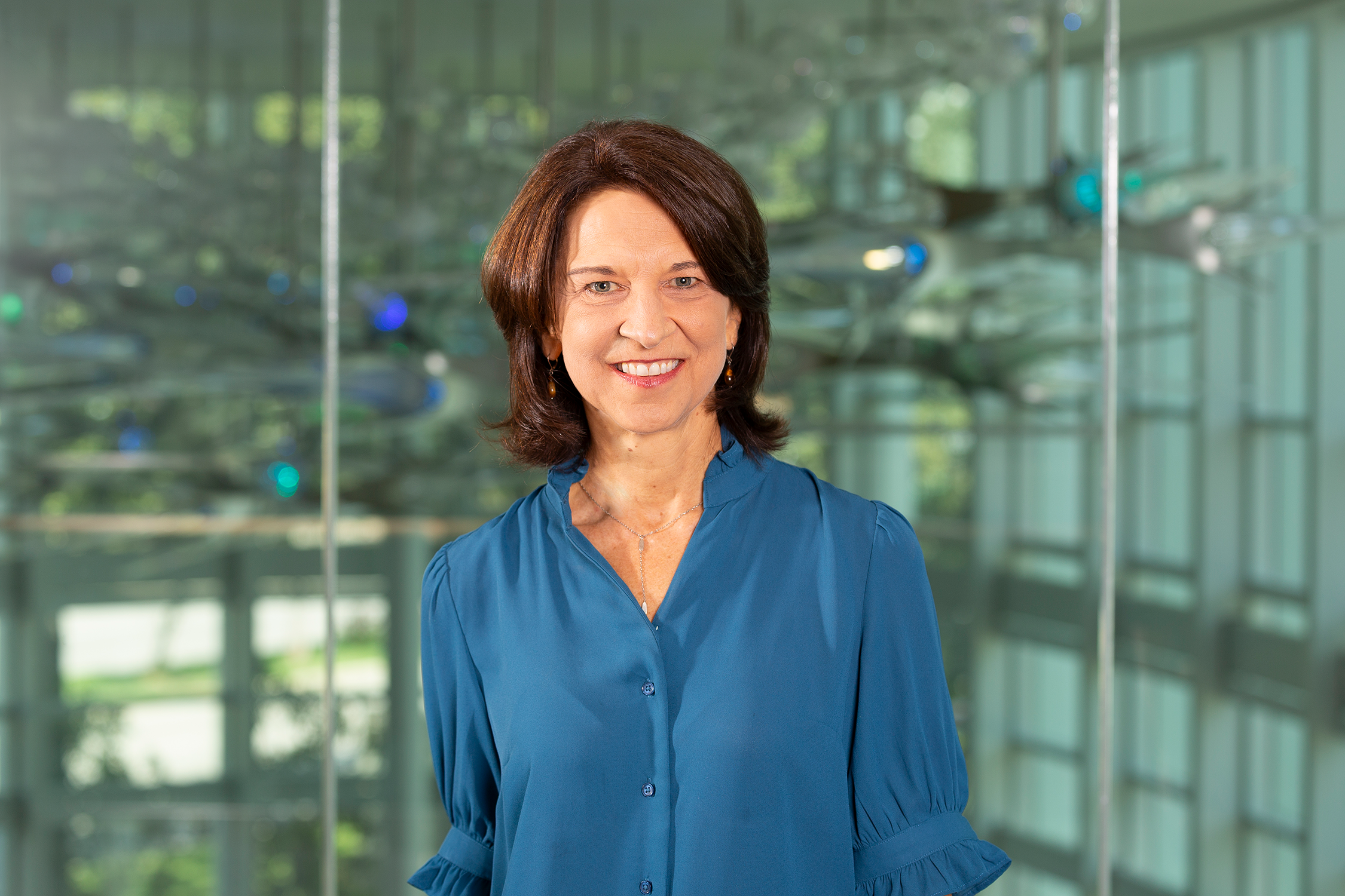 Headshot of researcher and program coordinator Janet Koslovsky, MS, at Center for BrainHealth, with a glass sculpture of illuminated neurons in the background. 