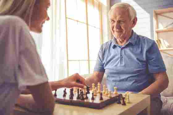 A smiling woman is playing chess with a smiling elderly male in a house setting. IStock# 619393614.
