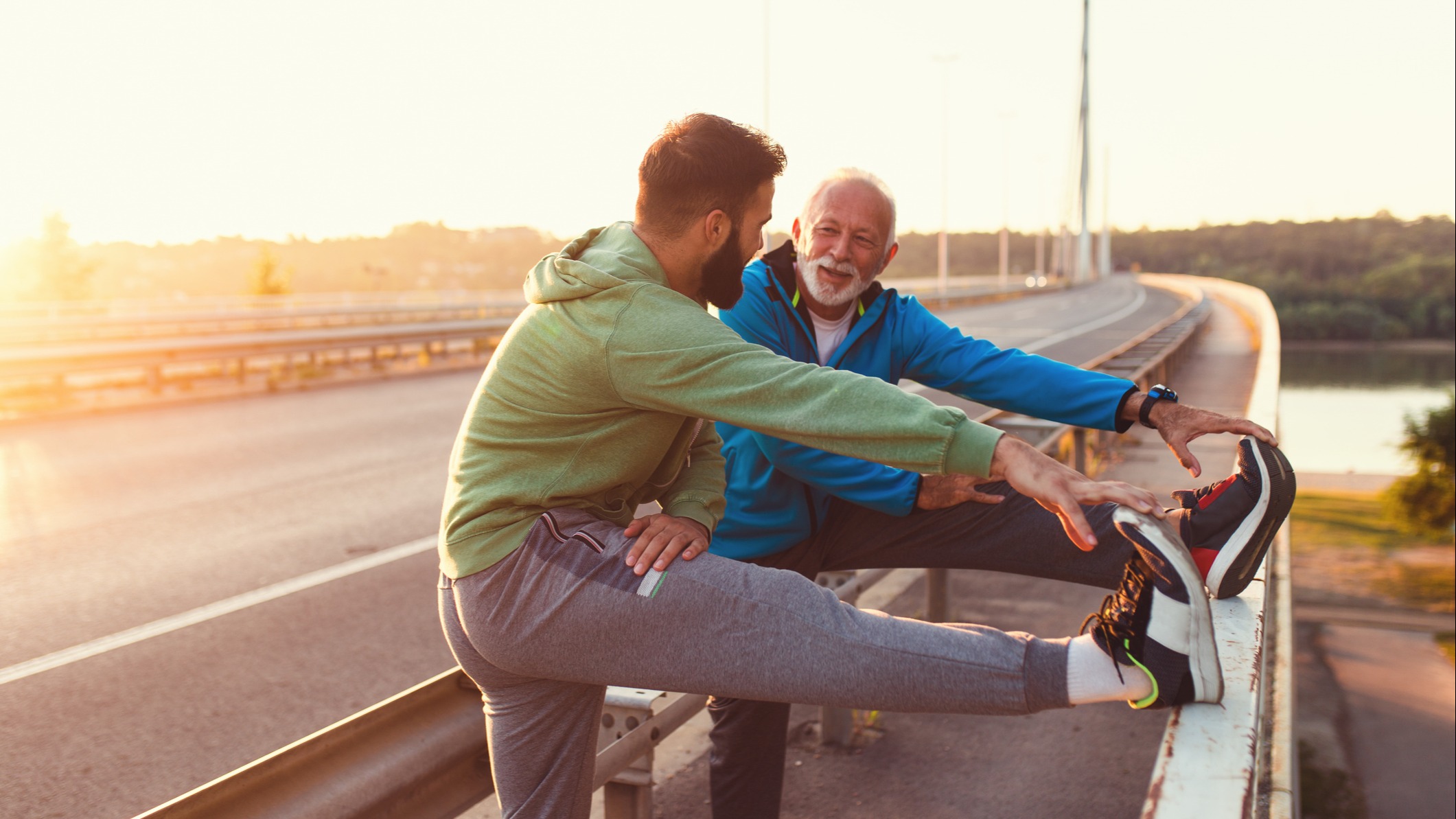 A father and son stop to stretch and encourage each other by the side of an exercise path. 