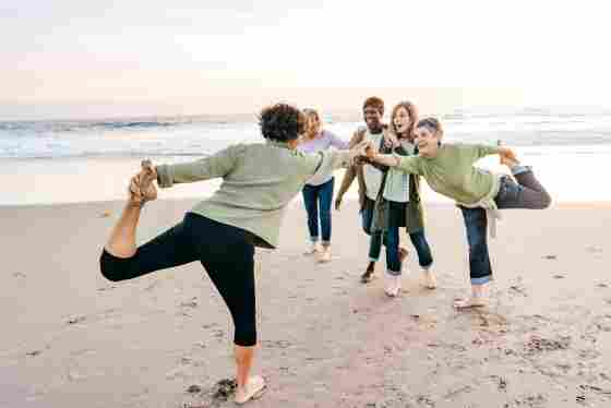 Five happy women in their 60s doing stretching exercises on the beach.