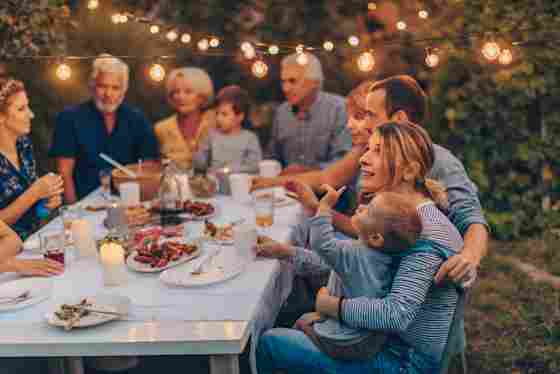 A multi-generational family enjoys Thanksgiving beneath festive lights in their backyard.