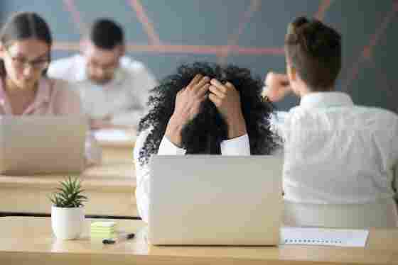 Frustrated worker at laptop, holding head in hands.