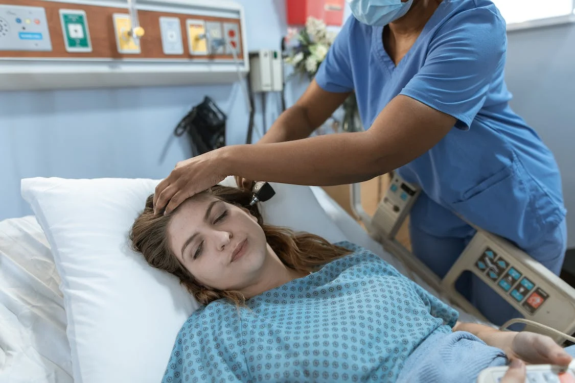 Women in hospital bed being tended to by a person of color