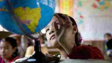 A child studies a globe of Earth in a classroom.