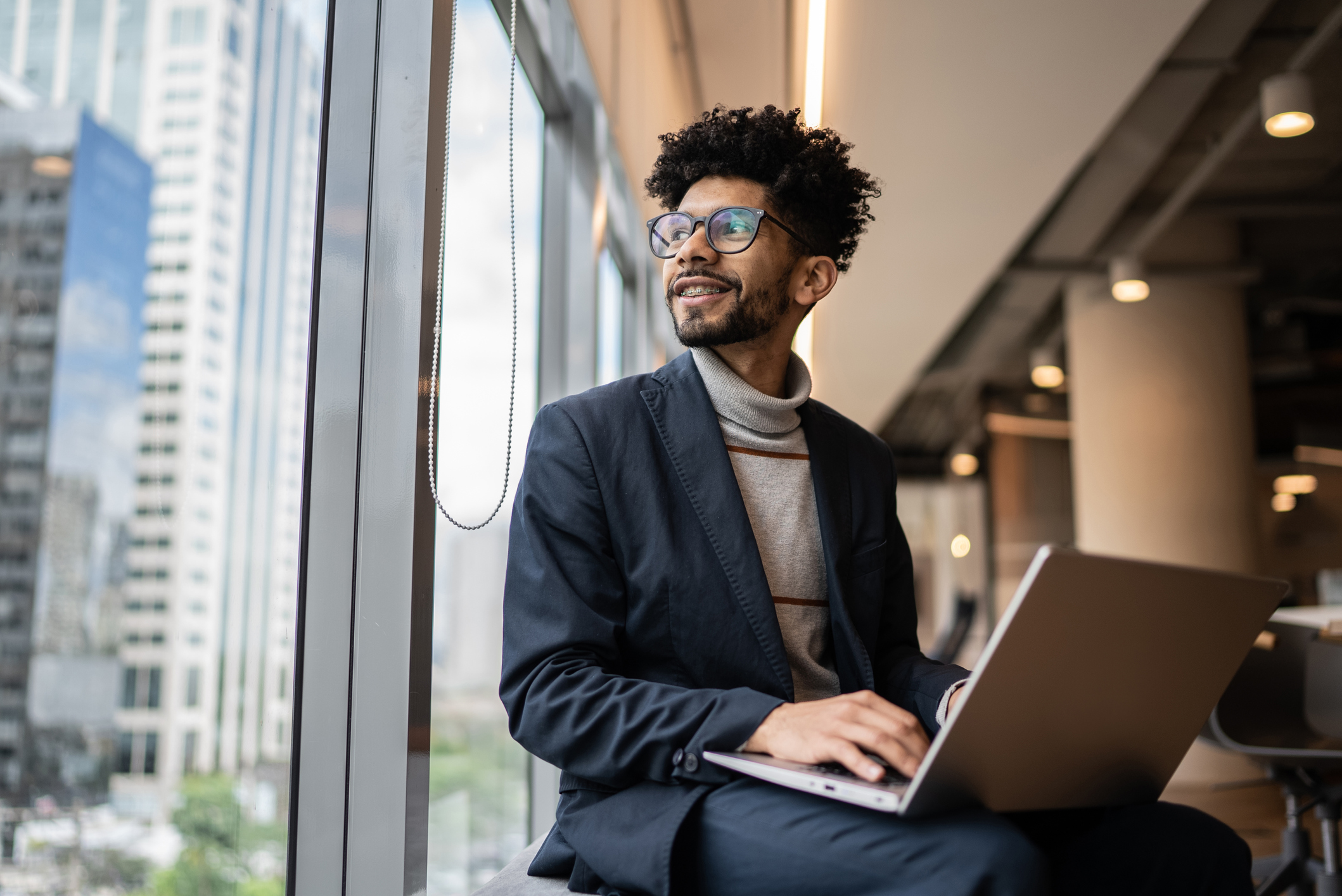 Businessman contemplating in the office looking through the window working on a laptop