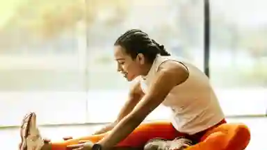 A woman of color stretching by a sunlit window before yoga class.