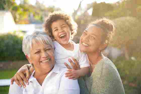 Portrait of happy and laughing grandmother with adult daughter and grandson relaxing in their garden