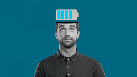 A man looks up at a full battery icon emerging from his open head, symbolizing mental energy, on a teal background.