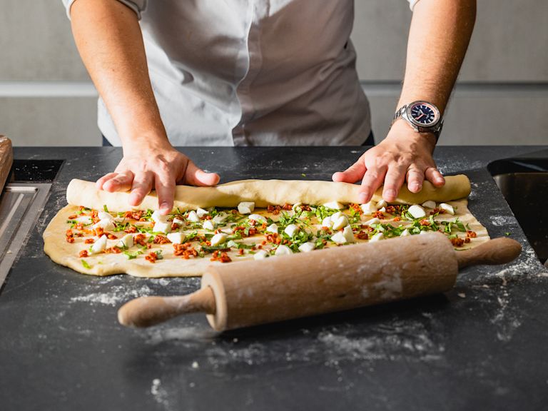 Schritt 2: Den Teig von der langen Seite her aufrollen und in der Mitte längs durchschneiden. Schritt 2: Den Teig von der langen Seite her aufrollen und in der Mitte längs durchschneiden.