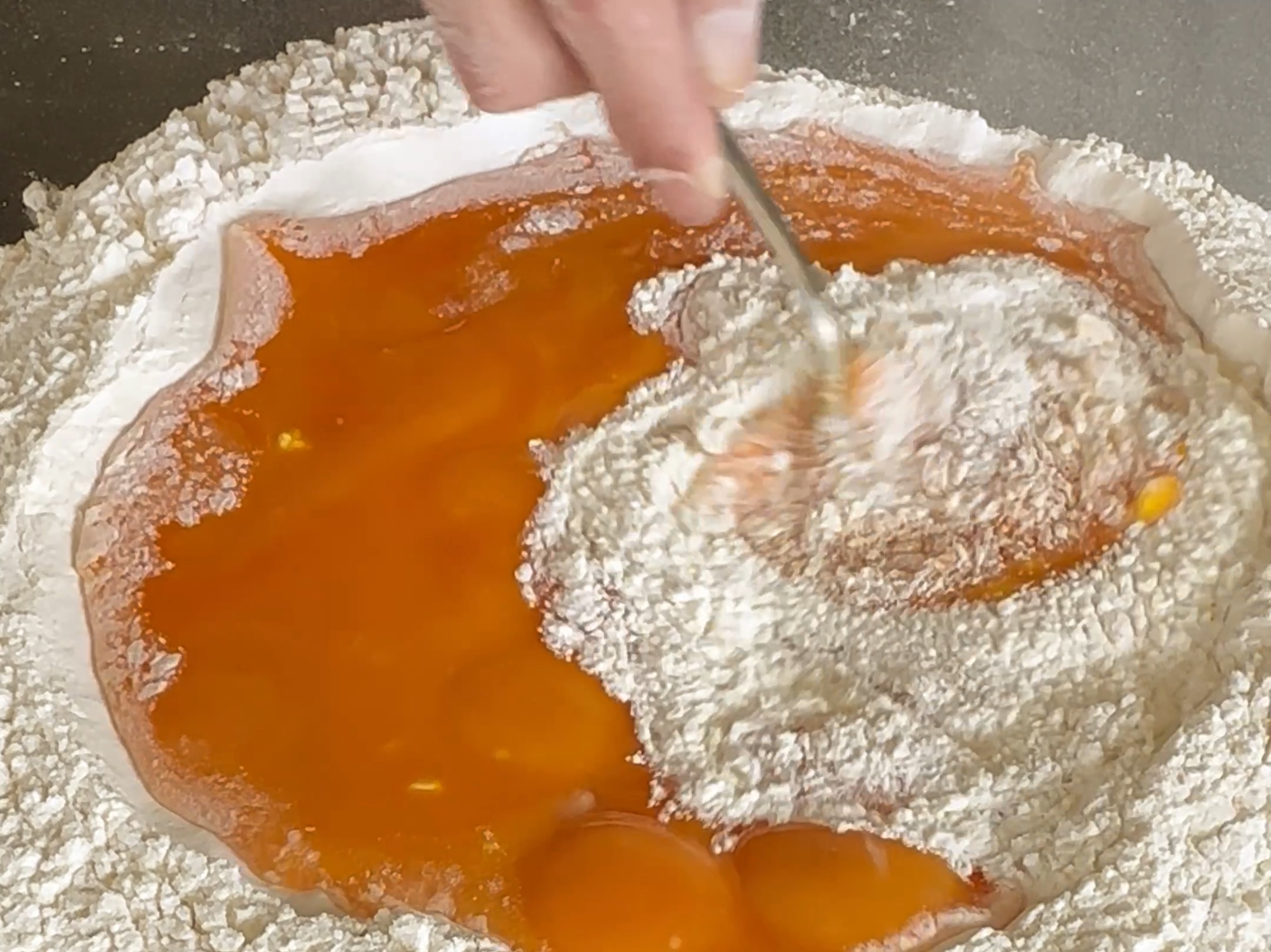 Schritt 1: Das Eigelb nach und nach in die Mulde geben und mit den Fingern kreisförmig in das Mehl einarbeiten, bis ein feuchter Teig entsteht
