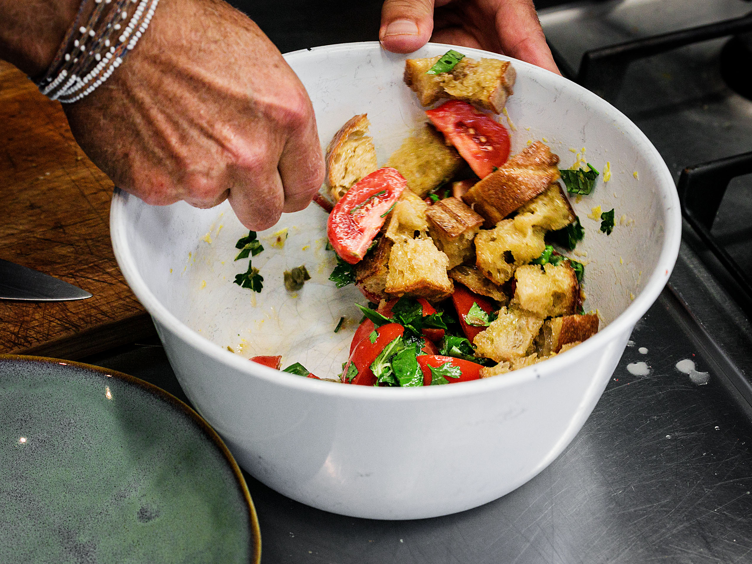 Schritt 3: Tomaten, Zitronenabrieb, Zitronensaft, Kapern, drei Viertel der Petersilie und drei Viertel des Basilikums zu den gerösteten Brotwürfeln in die Schüssel geben und alles vorsichtig vermischen