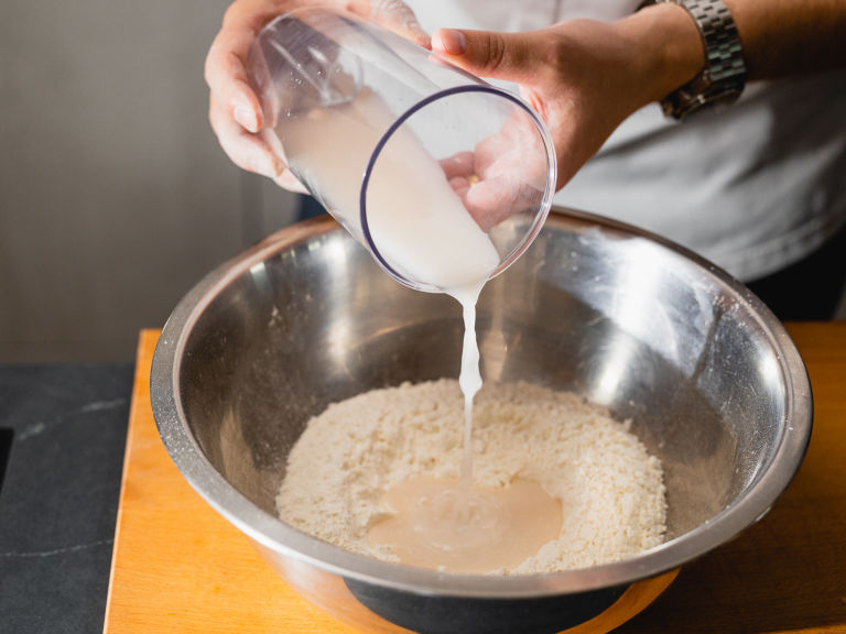Schritt 1: Gib die Hefe-Wasser-Mischung zum Mehl und knete den Teig ca. 10 Minuten lang mit den Händen oder einem Handrührgerät mit Knethaken, bis er glatt und elastisch ist.  