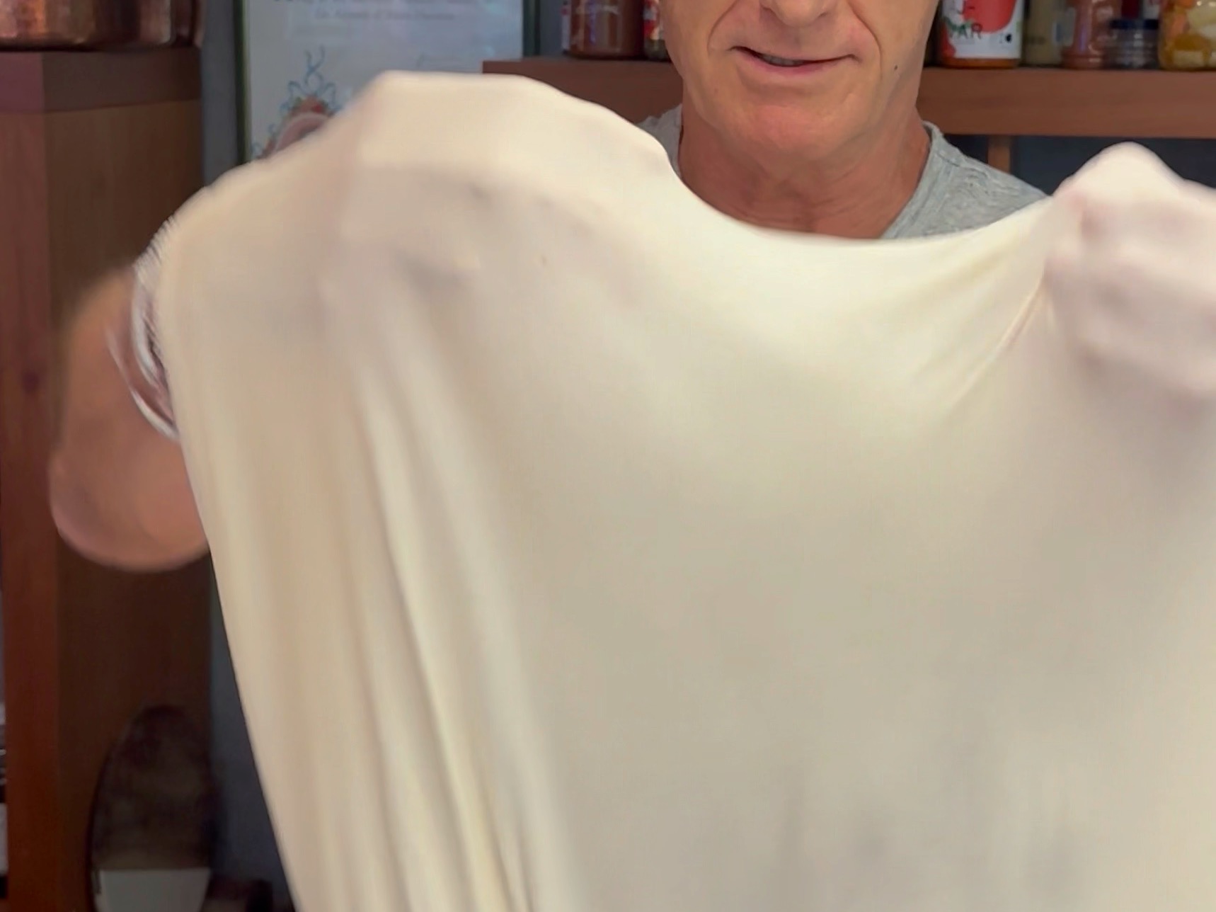 Schritt 2: Die Teigballen auf einer bemehlten Arbeitsfläche leicht ausrollen, dann über die Fäuste legen und rotierend auseinanderziehen, bis der Teig durchscheinend dünn wird