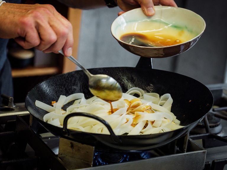 Schritt 5: Die Reisnudeln in die Pfanne geben und schwenken, dann 3 Esslöffel Sauce dazugeben und unter Rühren braten