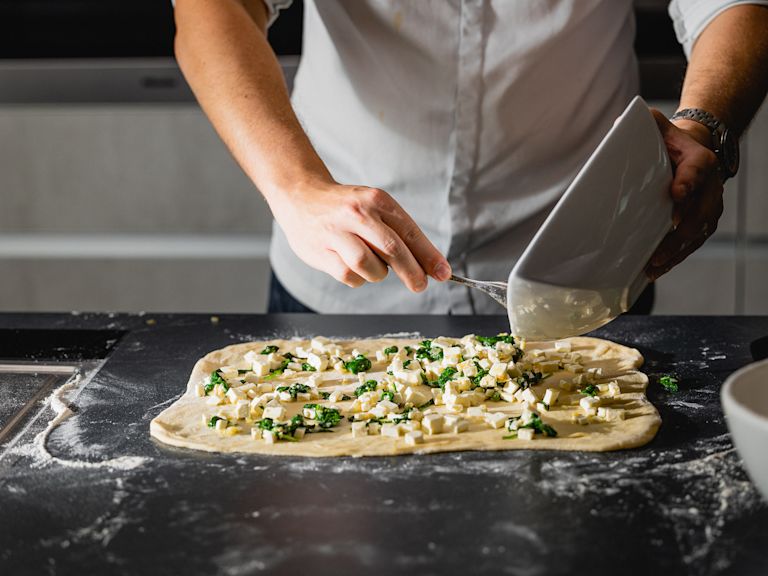 Schritt 2: Den Teig auf einer bemehlten Arbeitsfläche zu einem Rechteck ausrollen und die Spinat-Feta-Mischung darauf verteilen. Schritt 2: Den Teig auf einer bemehlten Arbeitsfläche zu einem Rechteck ausrollen und die Spinat-Feta-Mischung darauf verteilen.