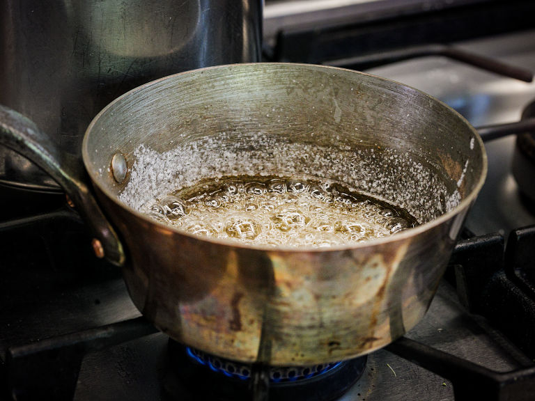 Schritt 2: Zucker und Wasser zum Kochen bringen und ohne Rühren kochen, dabei den Topf gelegentlich umrühren, bis die Masse dunkel karamellisiert.