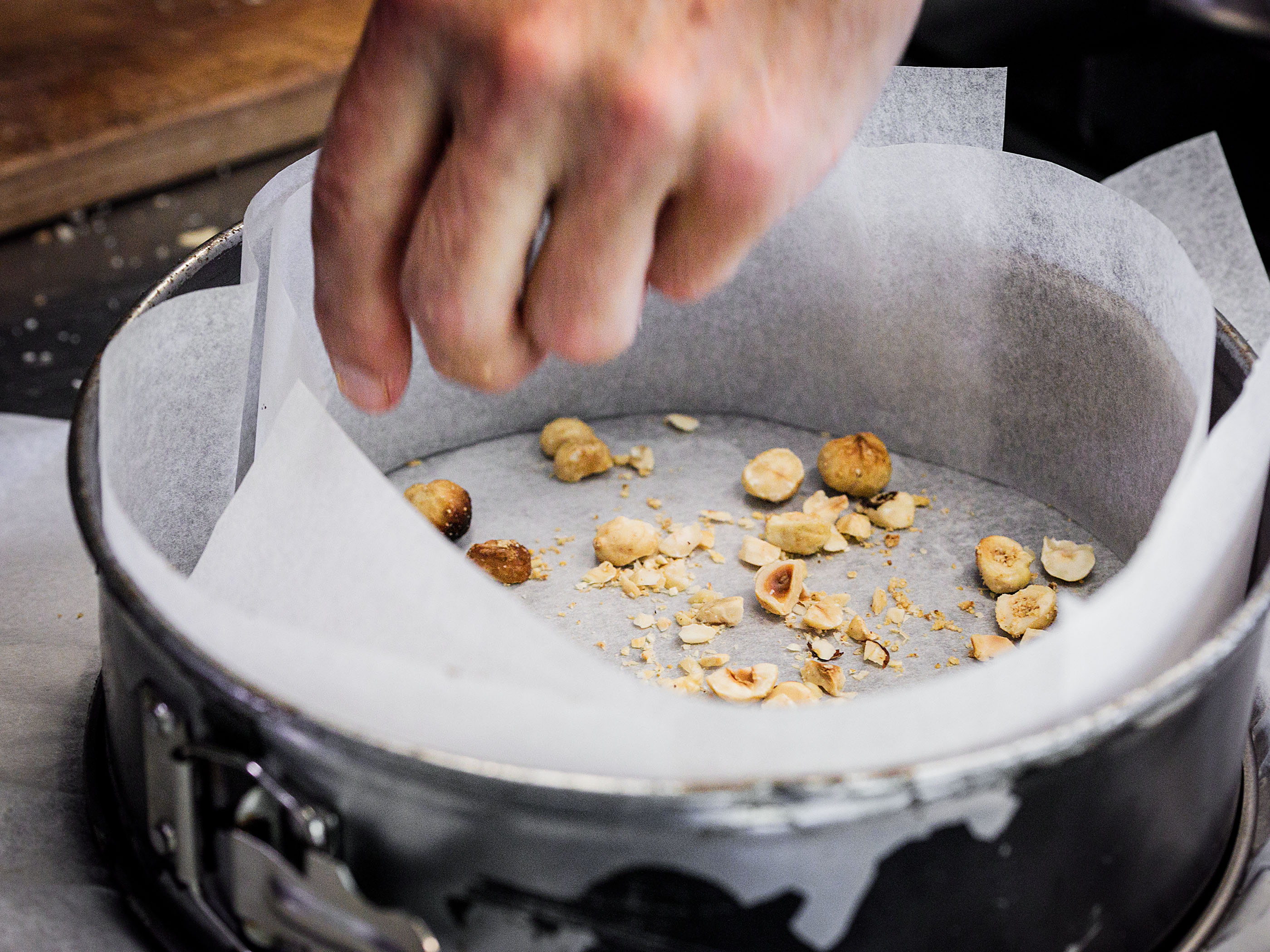 Schritt 2: Eine Handvoll der gröberen Haselnussstücke herausnehmen und auf dem Boden der Kuchenform verteilen