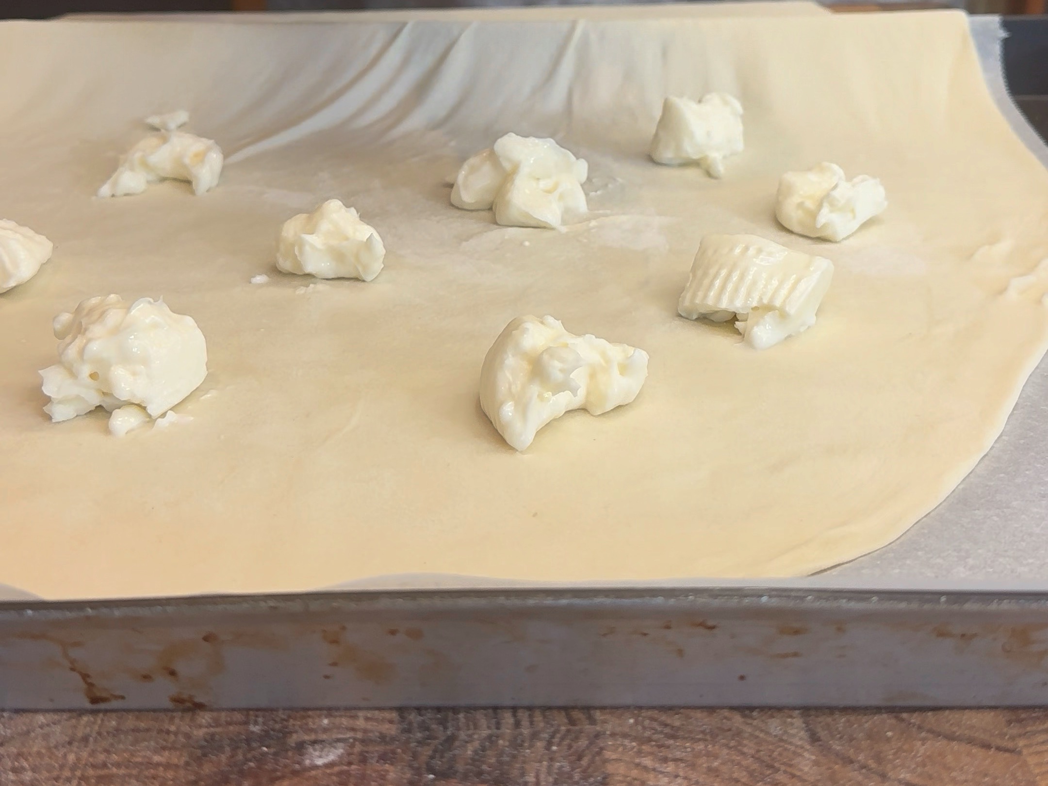 Schritt 2: Den ausgezogenen Teig auf ein geöltes Backblech legen und mit Stracchino-Stückchen belegen