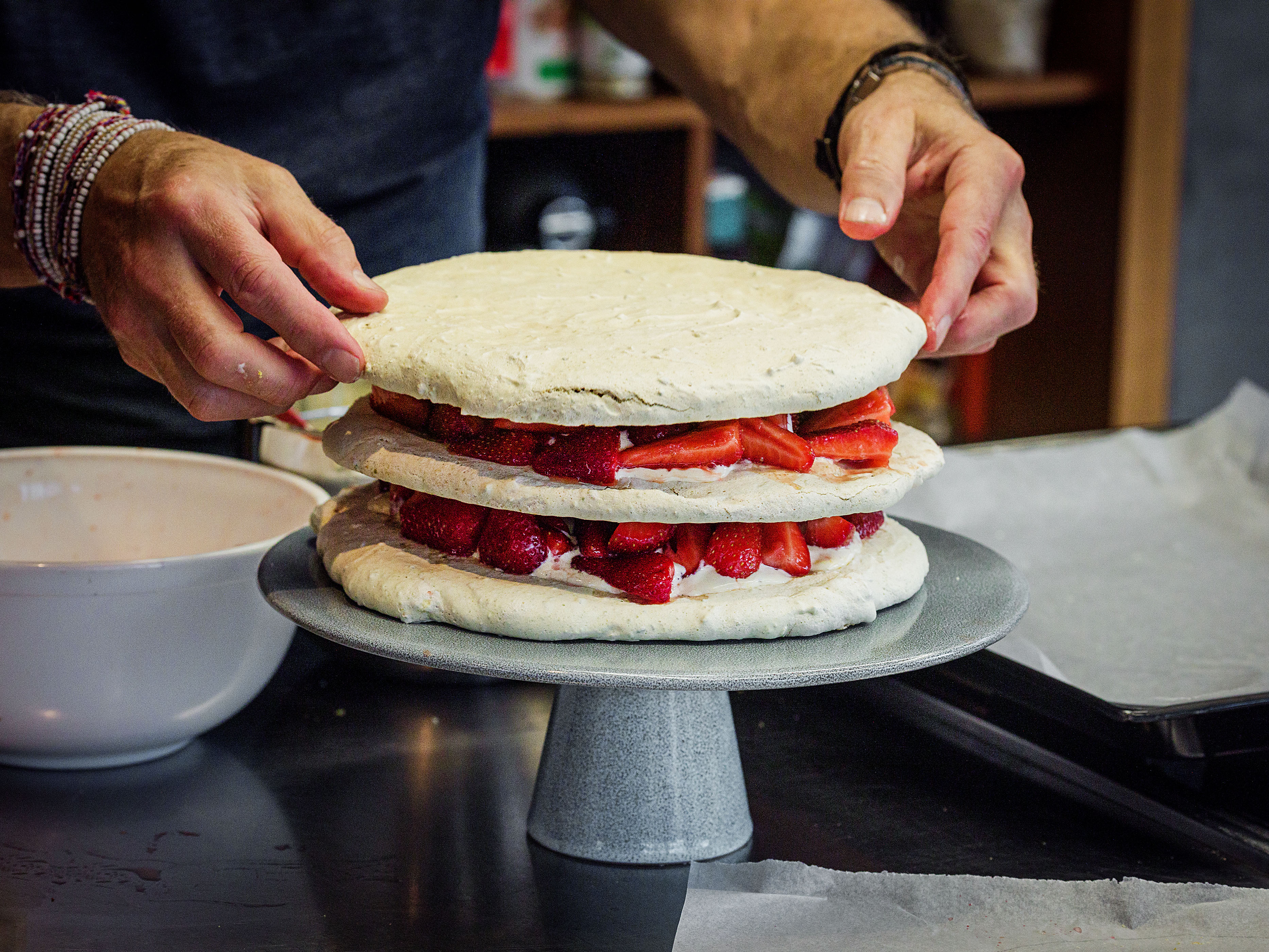 Schritt 4: Eine Meringue-Scheibe auf eine Platte legen, ein Drittel der Creme gleichmässig darauf verteilen, ein Drittel der Erdbeeren darüber streuen und mit den anderen 2 Scheiben gleich verfahren