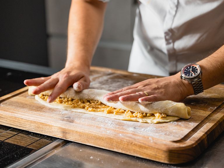 Schritt 2: Den Teig von der langen Seite her aufrollen und in der Mitte längs durchschneiden. Die beiden Teile übereinanderlegen und den Zopf flechten. Schritt 2: Den Teig von der langen Seite her aufrollen und in der Mitte längs durchschneiden. Die beiden Teile übereinanderlegen und den Zopf flechten.