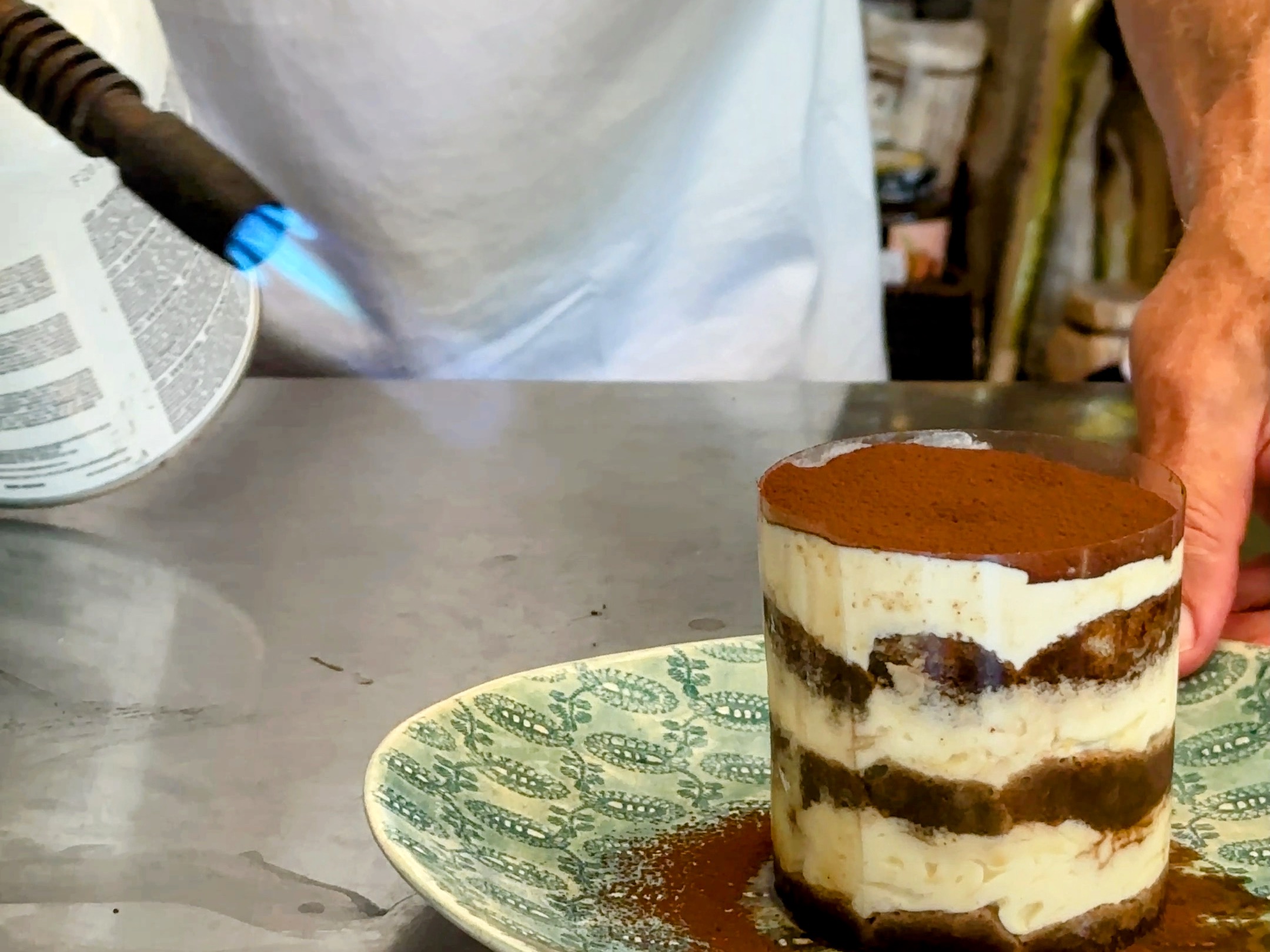 Schritt 4: Wenn das Tiramisu zu kalt ist und sich deshalb die Folie nicht löst, das Tiramisu mit einem Bunsenbrenner von der Seite her vorsichtig erwärmen