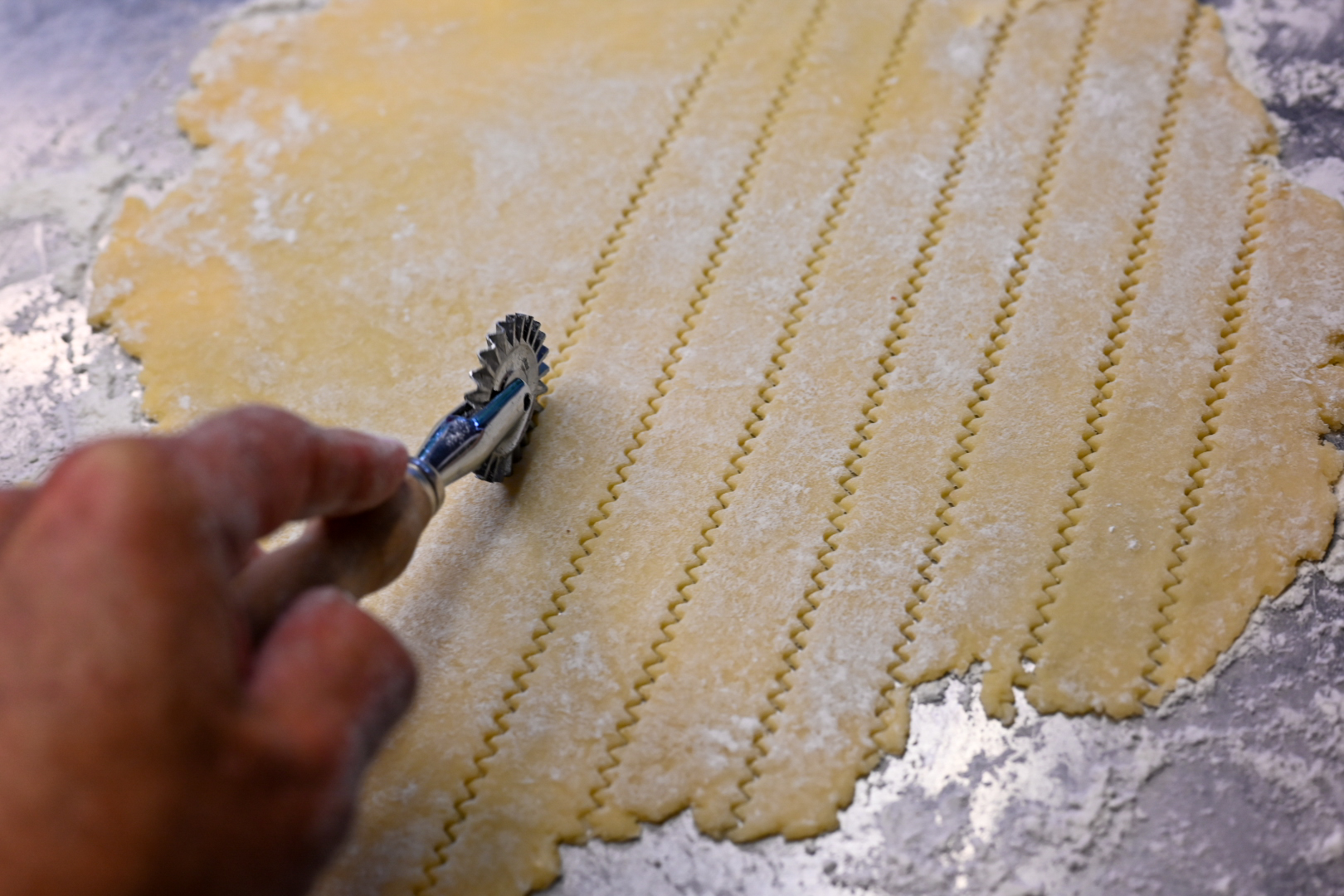 Schritt 2: Die kleinere Teigscheibe ebenfalls auf leicht bemehlter Arbeitsfläche 3 mm ausrollen und 22 cm rund ausrollen, mit einem Teigrädchen in 14 x 1,5 cm breite Streifen schneiden