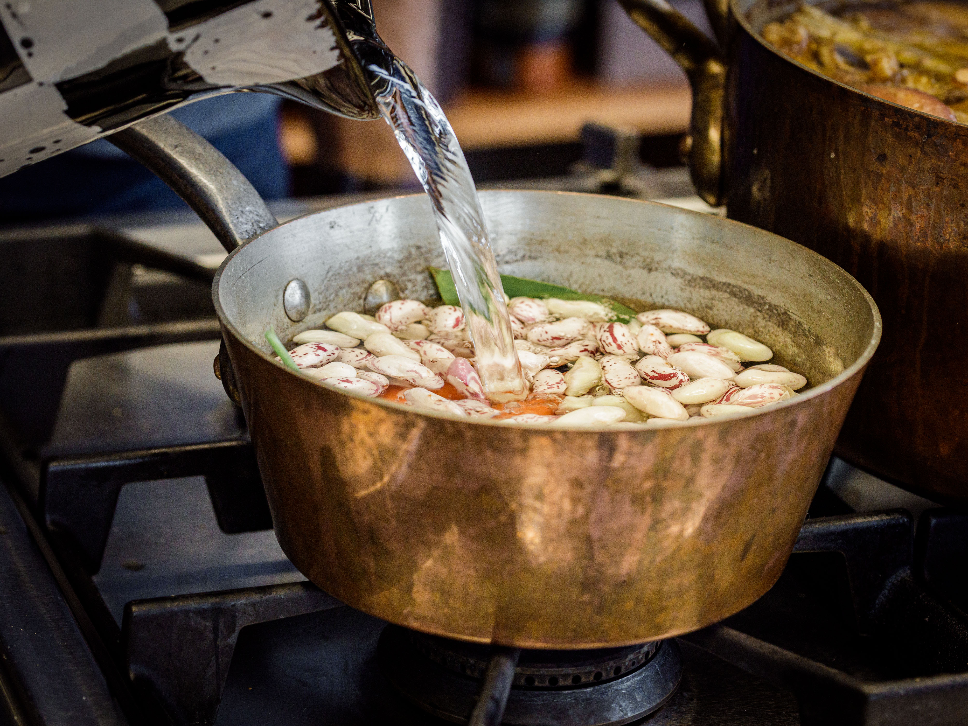 Schritt 2: Das Gemüse mit den Bohnen, den Stängeln der Petersilie, Lorbeer, den Knoblauchzehen und 2 Teelöffel Meersalz in einen grossen Topf geben und mit kaltem Wasser auffüllen