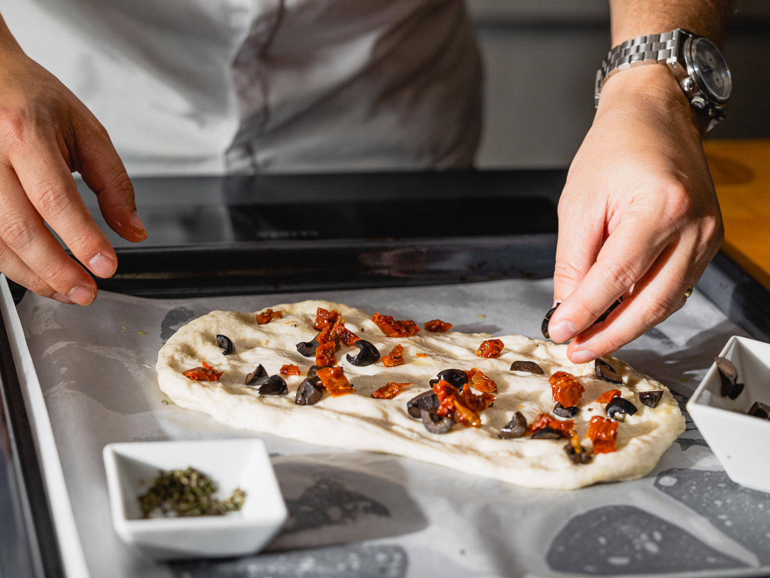 Schritt 2: Drücke mit deinen Fingern kleine Mulden in den Teig und verteile die Oliven und getrockneten Tomaten darauf