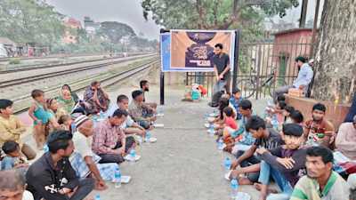 A large group of people, including men, women, and children, sit in rows at the Feni railway station area, waiting to break their fast as part of a mass Iftar programme organised by Runner Bangladesh Development Society.