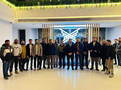 A group photo of the Runner Bangladesh Development Society delegation in front of the TÜGVA logo, showcasing the official visit and diplomatic engagement between the two organizations.