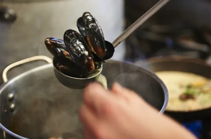 Moules being taken from a steaming saucepan
