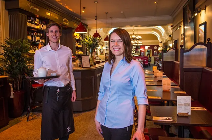Two smiling servers at the front of a restaurant