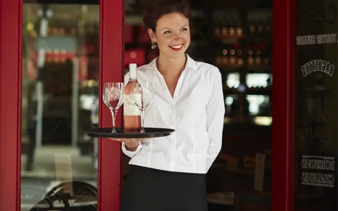 Smiling server carrying a tray of wine outside of a Cafe Rouge restaurant