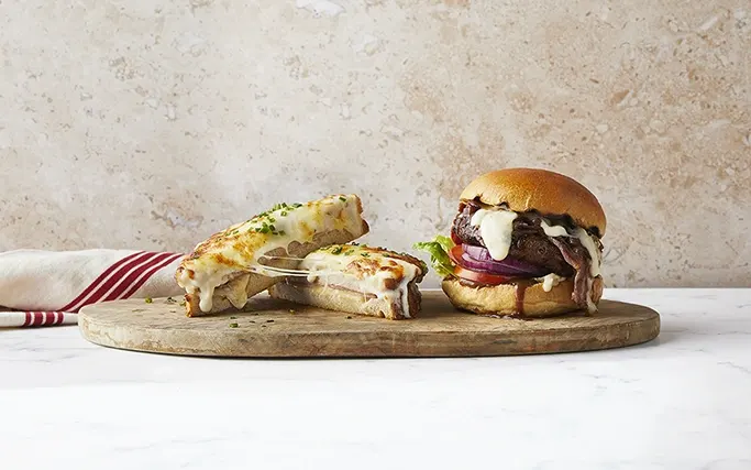 A cheesy croque and a burger on a wooden board