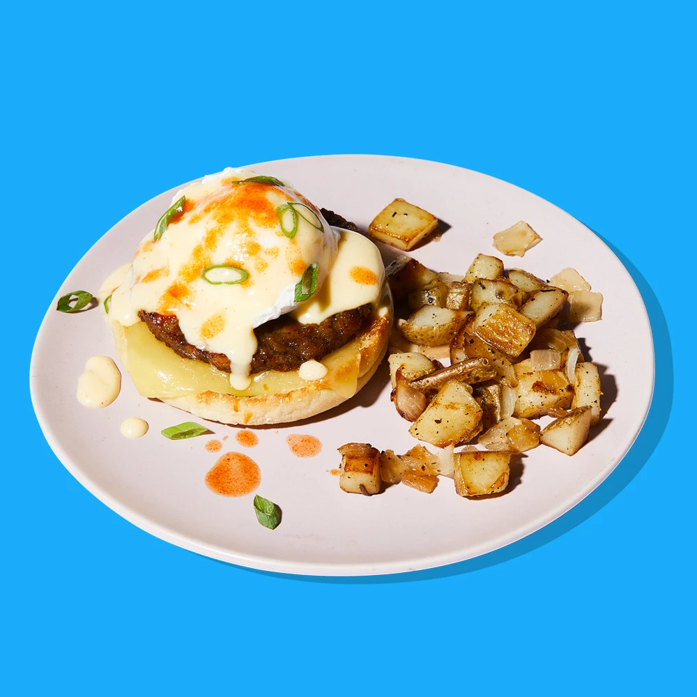 Impossible™ Sausage Benedict topped with hollandaise sauce, green onions, and hot sauce, served with crispy potatoes. 