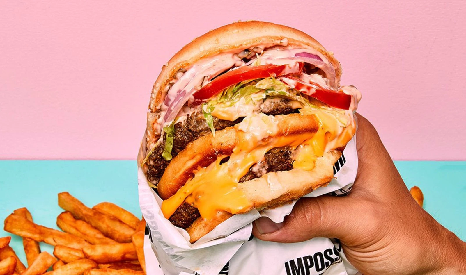 Veg News Impossible Burger with fries on pink and blue background