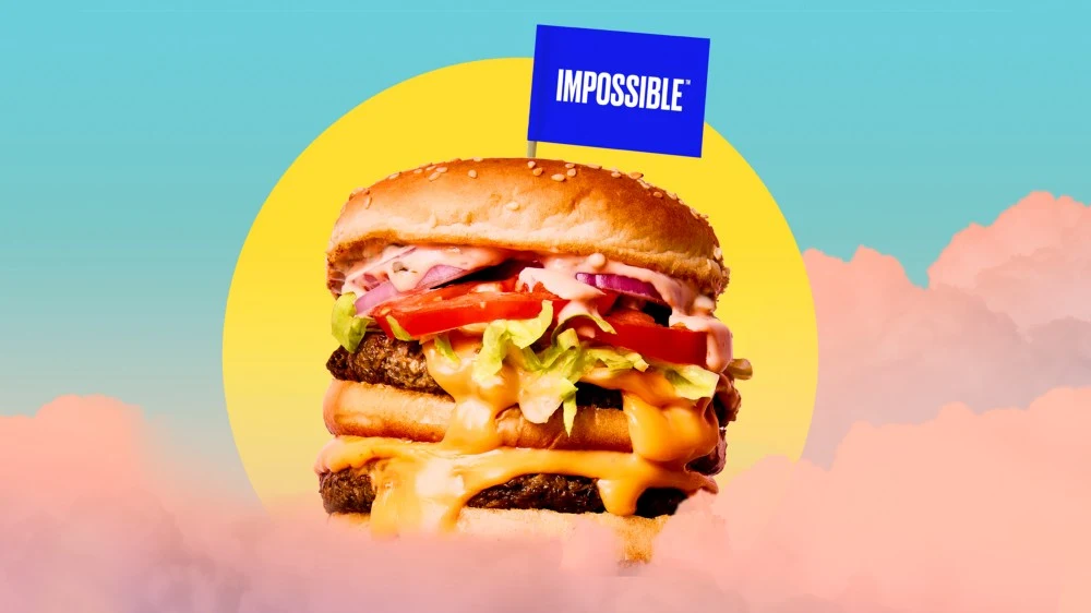  Impossible™ Burger with melty cheese and toppings, plus an Impossible flag, floating in the sky with the sun in the background.