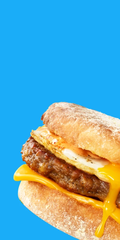 An Impossible Sausage breakfast sandwich dripping with egg and cheese on a blue plate and blue background