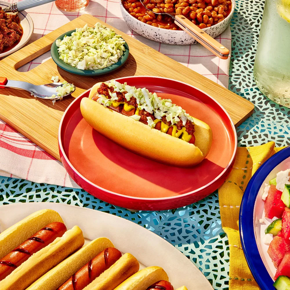 Impossible™ Carolina Slaw Dog on an orange plate on an outdoor picnic table. 