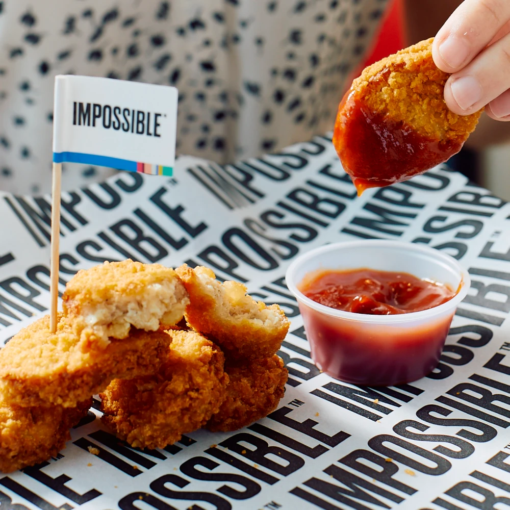 Image of a person dipping an Impossible Chicken Nugget into a container of ketchup
