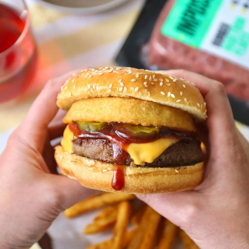 Two hands holding a burger with bbq sauce and cheddar cheese on a sesame bun.